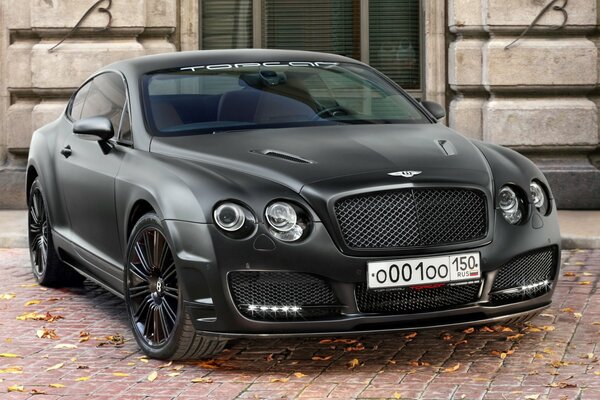 A black Bentley on a paving stone with fallen leaves