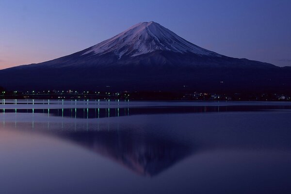 The mountain, at the foot of which the lights are burning, is reflected in the calm water