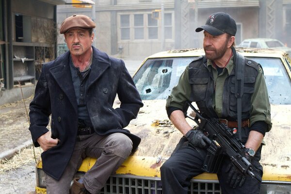 Two men are sitting on the hood of a wrecked car