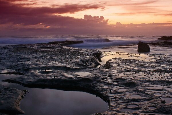 Extraordinary waves in the evening against the background of clouds and rocks