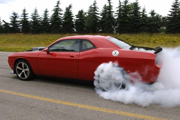 Red dodge challenger in smoke on the road in the woods