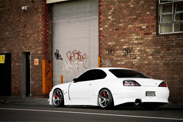 A white Nissan S15 Silvia stands against the background of a brick building