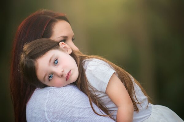 Niña de ojos azules yace con la cabeza sobre el hombro de su madre