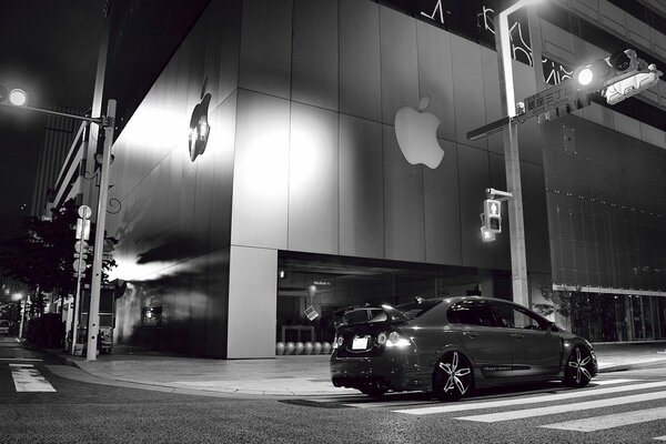 Foto en blanco y negro de un coche cerca del edificio apple