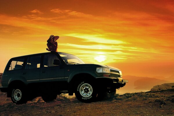 A girl on the roof of a jeep against the sunset