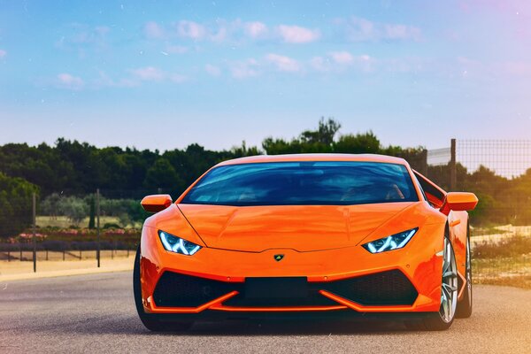 Pomarańczowa Lamborghini Huracan jedzie drogą na tle lasu