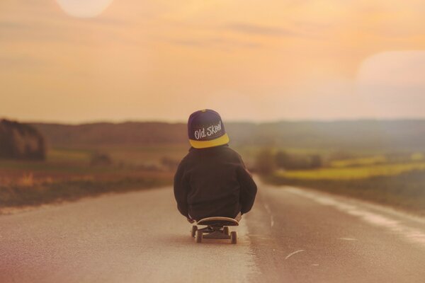 Ragazzo su uno skateboard che guarda il tramonto. Bellissimo tramonto rosso. Il ragazzo con il cappello cavalca lungo la strada