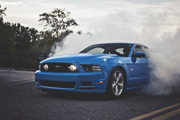 Un Ford Mustang azul en el camino hacia el humo