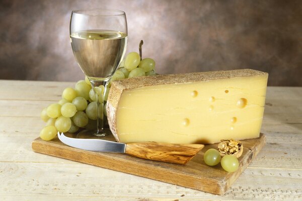 Weißwein in einem Glas mit einem Pinsel aus Trauben und köstlichem Käse