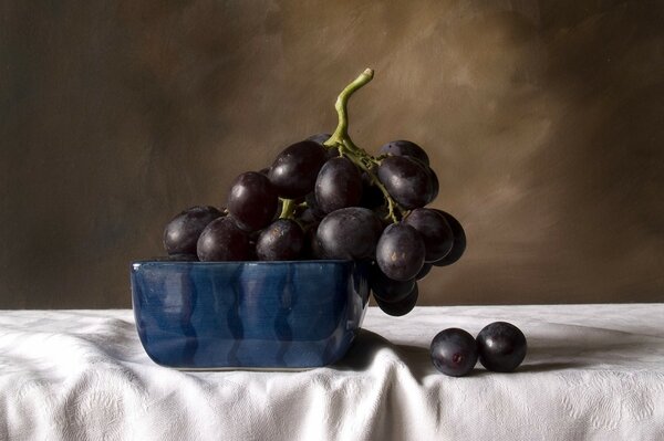 Still life of Black grapes in a blue bowl, on a white tablecloth