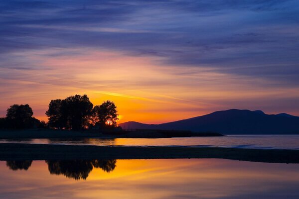 Orange sunset on the shore at the foot of the mountains