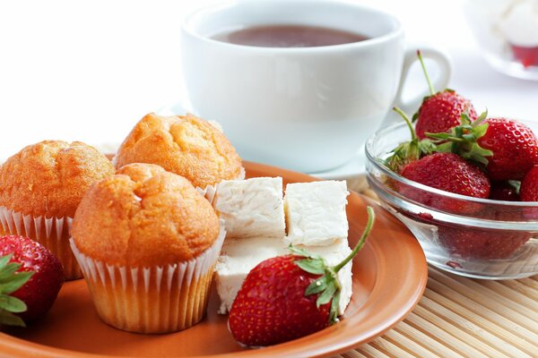 Cupcakes and strawberries on a plate . On the background of a cup of tea