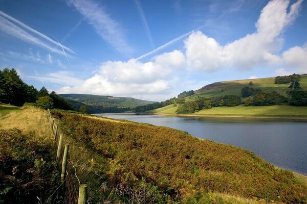 Paysage rustique. Rivière derrière la clôture et le ciel bleu clair