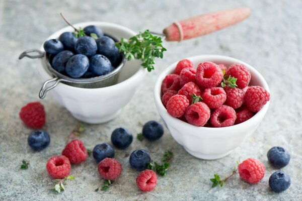 Himbeeren und Blaubeeren in weißen Porzellantassen