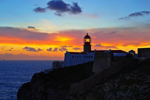 Faro in riva al mare su uno sfondo di tramonto e nuvole