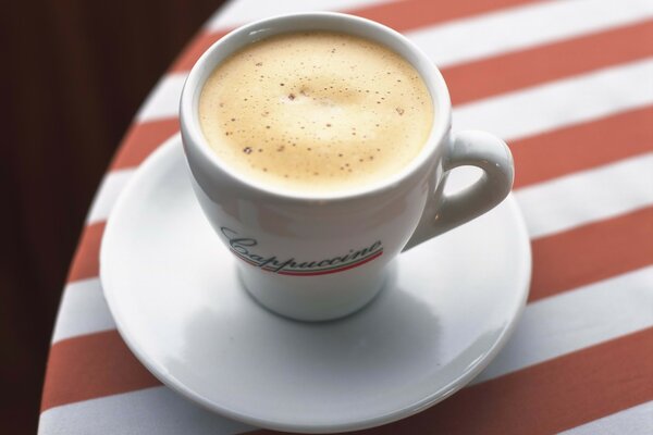 Cappuccino in einer weißen Tasse auf einer gestreiften Tischdecke