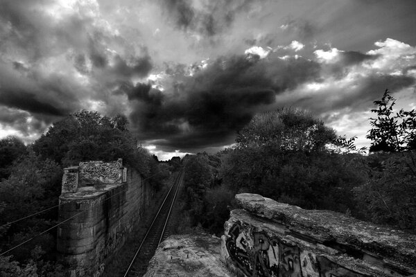 Immagine in bianco e nero con graffiti ferroviari e nuvole temporalesche