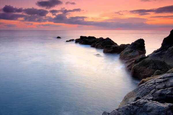 Ocean at the foot of the rocks, rocks at sunset, water in the ocean