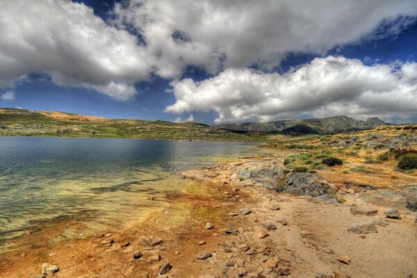 Ein felsiges Ufer am See und ein Himmel mit Wolken