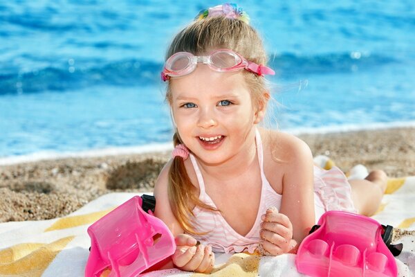 Fille aux yeux bleus sur la plage avec des lunettes de natation se trouve sur la plage et sourit