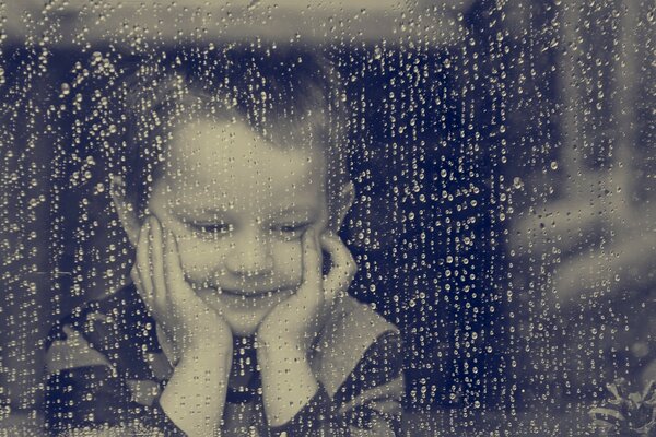 The boy looks out the rainy window