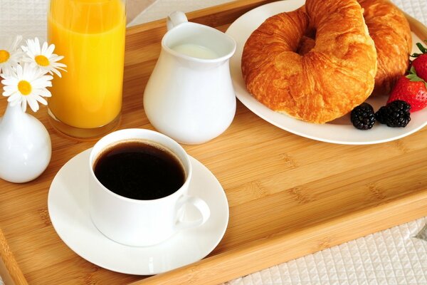 Una taza de café con cruasanes, bayas, leche y jugo de naranja servidos para el Desayuno en la cama