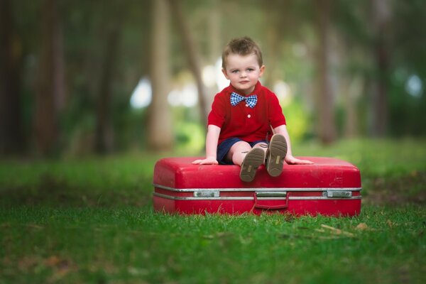 The boy is sitting on a red suitcase