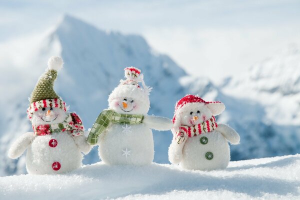 Drei kleine Schneemänner in Schals vor dem Hintergrund der Berge