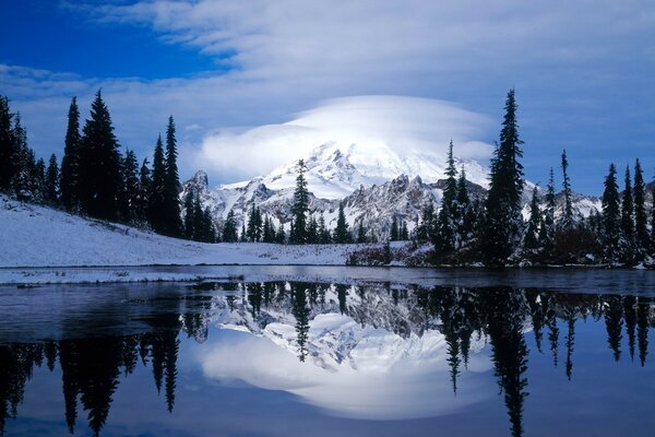 Volcan enneigé dans les nuages et les arbres se reflètent dans le lac