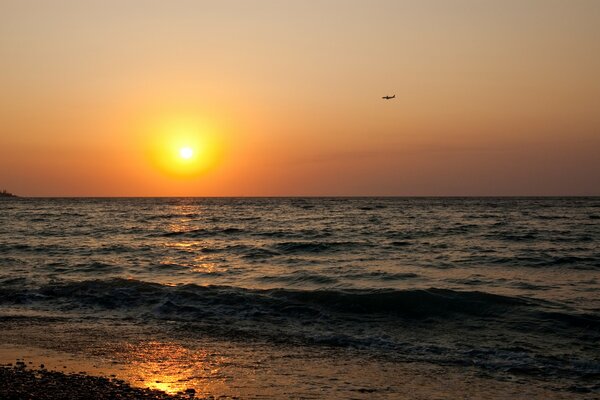 Puesta de sol en el mar con un avión en el cielo