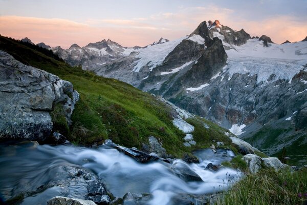 Ruisseau au milieu des montagnes enneigées et de l herbe