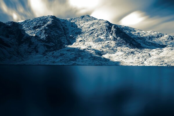 La superficie azul del mar en el fondo de las montañas cubiertas de nieve