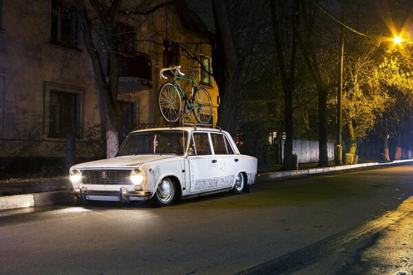 Un Lada blanco con una bicicleta en el techo por la noche espera al propietario