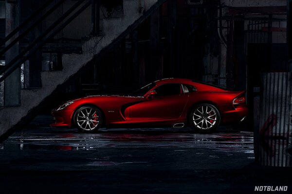 Red sports car under the stairs in a dark city after the rain