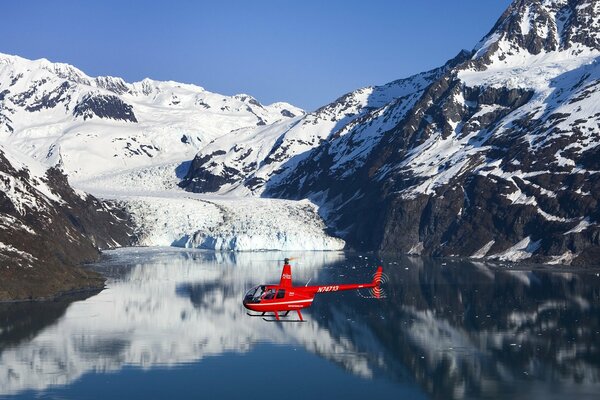 Red rescue helicopter over mountain lake