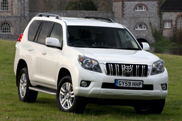 A white Toyota SUV stands majestically at the walls of the old castle in a green clearing