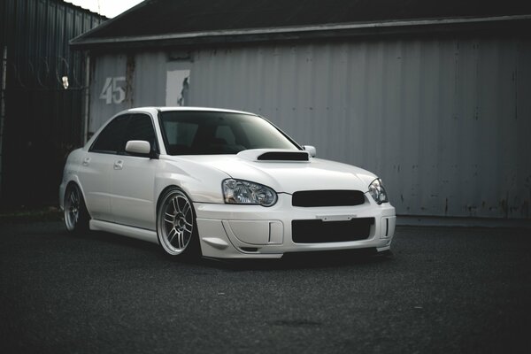 Wallpaper with a white subaru wrx on a background of gray garages