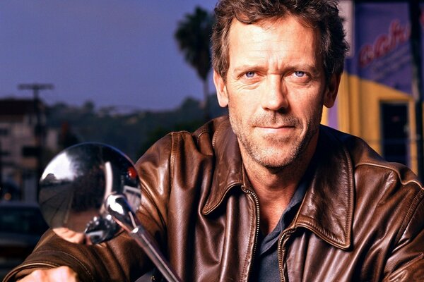 Hugh Laurie in a leather jacket on a motorcycle