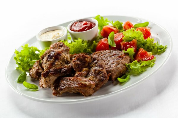 Fried meat on a white plate with vegetable salad and sauces