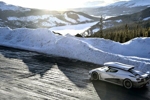 Biały Koenigsegg Agera ściga się po zaśnieżonej drodze w górach