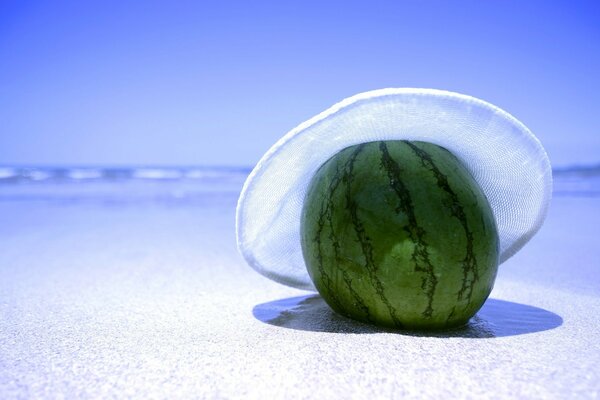 Eine einsame Wassermelone am Sandstrand mit einem gewöhnlichen Hut