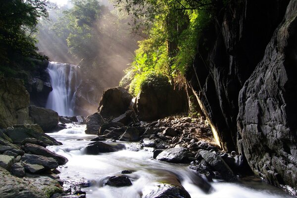 I raggi del sole illuminano la cascata tra le rocce