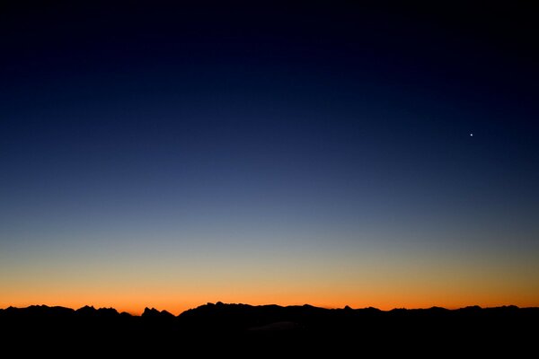 A strip of black horizon against the background of the orange line of the rising sun and the blue of the sky turning into night