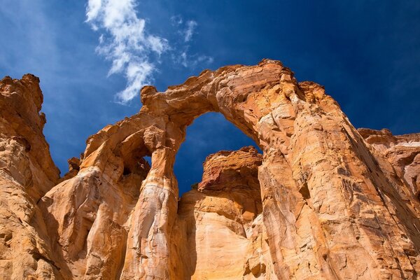 Arco in roccia arancione contro il cielo blu con nuvole bianche chiare