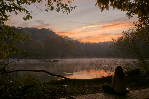 A lonely girl meeting the dawn on the shore of the lake