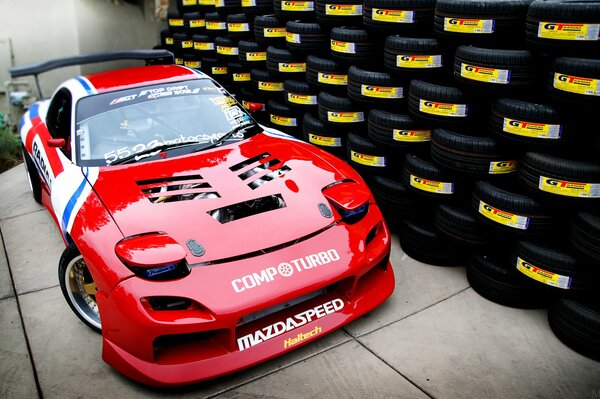 Roter Mazda rx- 7. moto tuning auf dem Hintergrund einer Wand aus Reifen