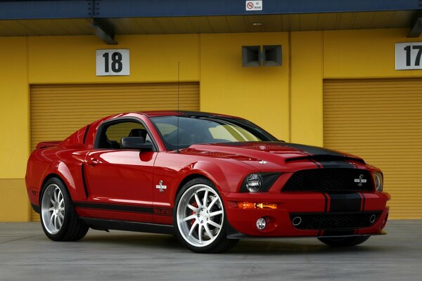 Red Ford Mustang standing next to the background of yellow garages