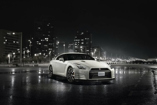 Biały Nissan gt-r na mokrym asfalcie na tle nocnego miasta