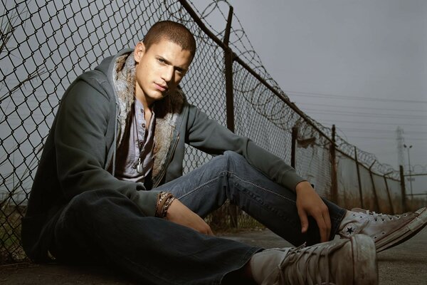 A handsome man is sitting by an iron fence net