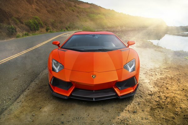 On an unlived highway near the river there is an orange Lamborghini